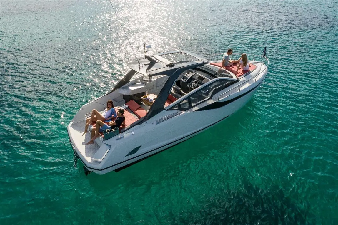 A white yacht with four people relaxing on board, surrounded by turquoise water and sunlight reflecting off the surface.